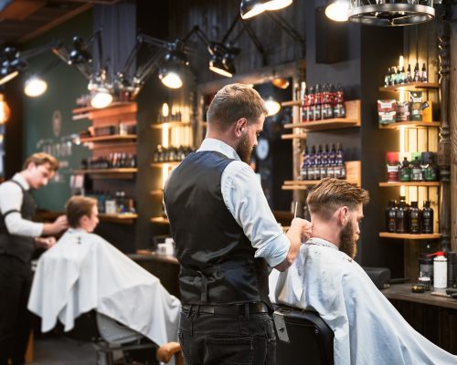 Professional barbers working on client hair in barbershop.